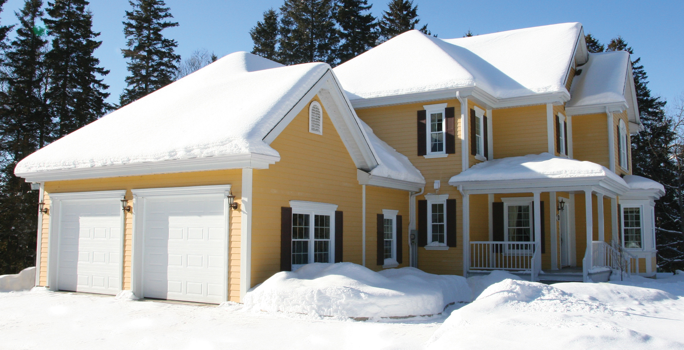 Traditional style yellow house in winter, with double garage having 9' x 7' Standard+ Classic CC Ice White garage doors.