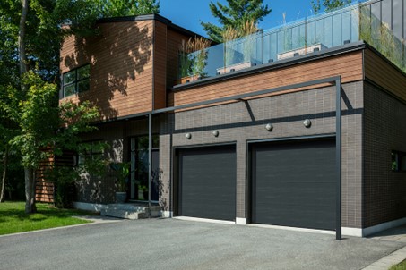 Maison moderne avec deux portes de garage de couleur Minerai de fer, un gris très foncé.