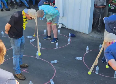 People at a Garaga Ponca facility party playing an outdoor game wearing pantyhose with tennis balls on their heads