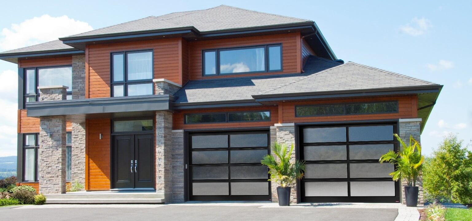 Maison en pierres de couleur gris-beige, avec vinyle orange brulé, agencés avec 2 portes de garage vitrées California avec verre Sablé.