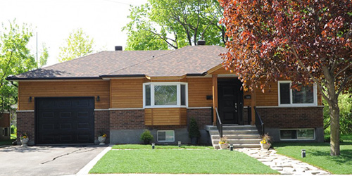Bungalow des années 70 rénové avec une touche plus moderne et ajout d’un garage attaché avec une porte de garage simple de couleur Noir.