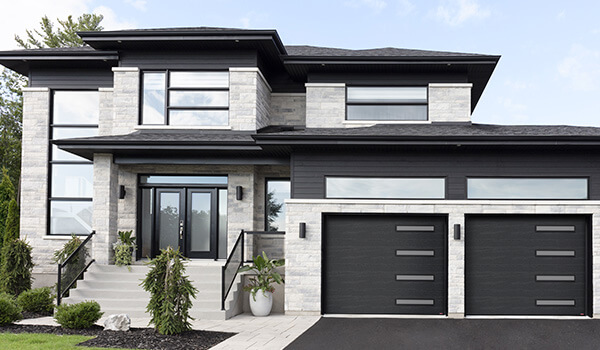 Maison deux étage, extérieur de style transitionnel, pierre gris chaud, accents charcoal et noir, larges fenêtres horizontales, portes de garage noires avec fenêtres étroites