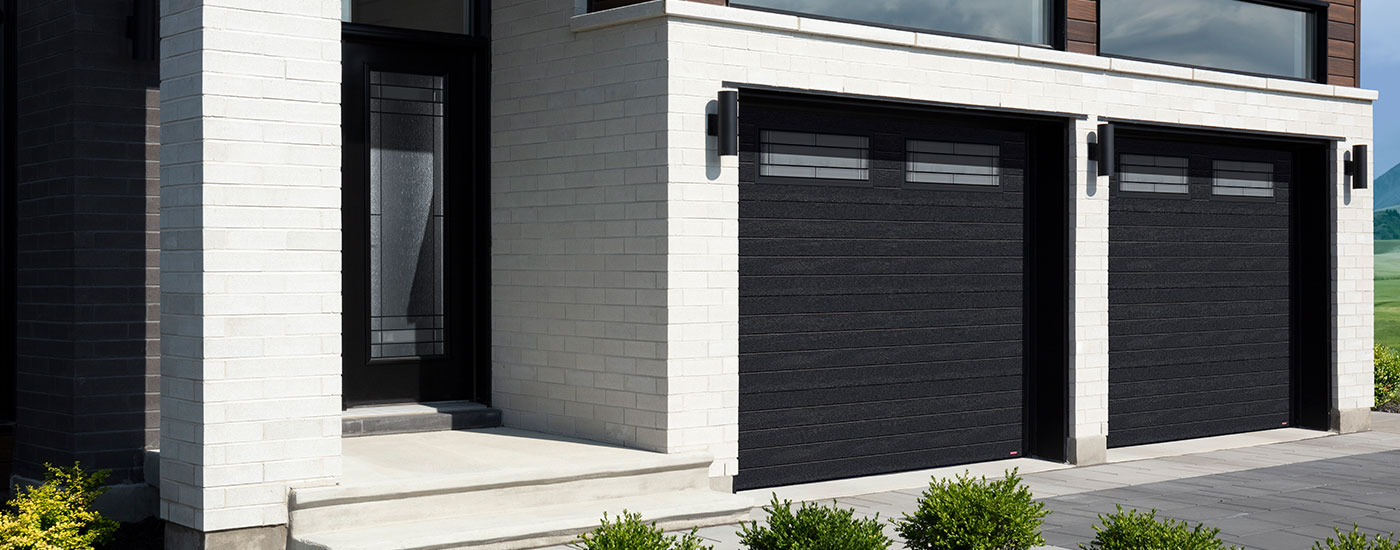 Maison contemporaire en brique gris pàle et bois brun foncé avec garage double attaché. Portes de garage modernes avec vitrail Céleste