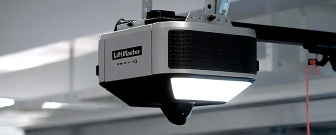 Close-up of a LiftMaster garage door opener mounted on the ceiling, emitting bright white light.