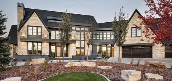 Large stone house in shades of beige with many windows and double Black garage door.