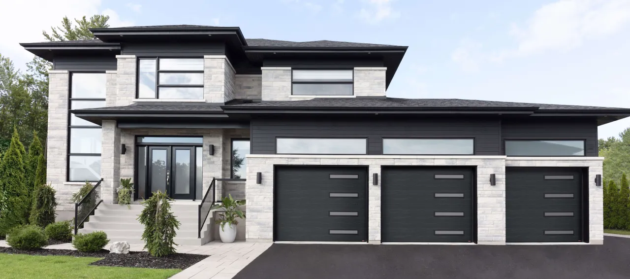 Contemporary 2-storey house in warm grey stone, dark grey wood, large windows, modern black entry door and three garage doors, with Slim windows