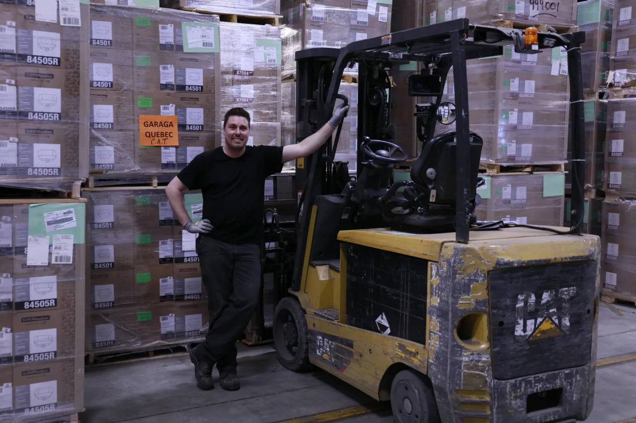 Employé souriant avec un lift dans l'entrepôt chez Garaga