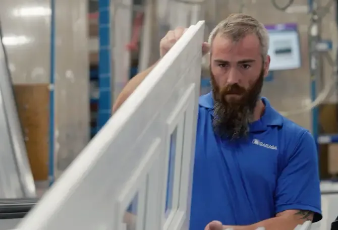 Journalier inspectant une section de porte de garage blanche dans l’usine de Garaga